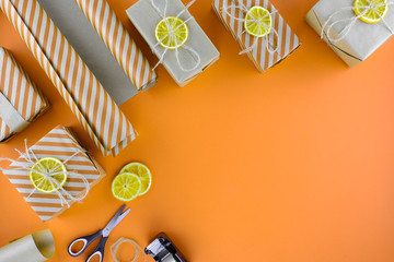 Preparing for Christmas gifts packaged. Boxes, wrapping paper and scissors on an orange background. Top view, copy space.