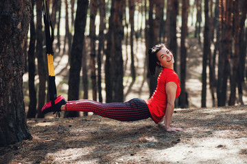 woman doing trx exercise with suspension trainer sling in the outdoors pine forest healthy - obrazy, fototapety, plakaty