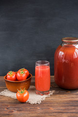 Tomato juice with tomatoes on black and wooden background.