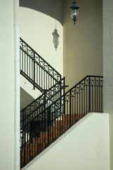 A lantern hanging in a zig-zag stairwell casts a shadow on the wall above the steps. Architectural image
