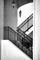 A lantern hanging in a zig-zag stairwell casts a shadow on the wall above the steps. Architectural image in black and white.