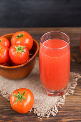 Tomato juice with tomatoes on black and wooden background.