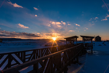 the sun sets behind the mountains and colors the clouds in winter, Altai, Russia