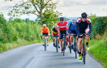 A group of cyclists on a bike race on a sunny day along country roads in the UK.