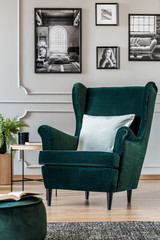 Pillow on emerald green armchair in elegant living room interior with black and white posters on...