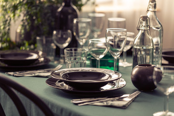 Closeup of elegant dining table with green tablecloth, black plates and wine glasses