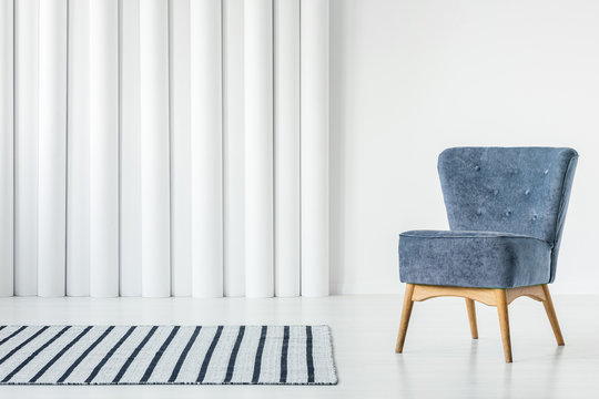 Trendy blue armchair in empty white interior with striped rug