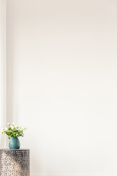 Copy space on empty white wall of elegant living room, coffee table with vase with flowers in the corner