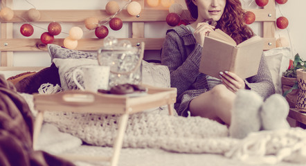 Woman reading book on bed with cotton balls on wooden headboard in bedroom interior