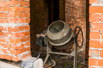 Old grey cement mixer against a brick wall.