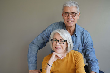  Portrait of relaxed fun senior couple wearing glasses on background