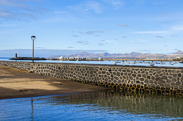  View of the footbridge Calle Punta de la Lagarta, small island Islote de Fermina and volcanoes of Lanzarote