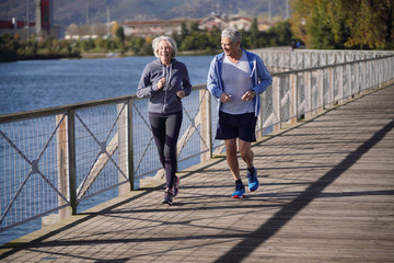  Active senior couple jogging together on bridge - obrazy, fototapety, plakaty