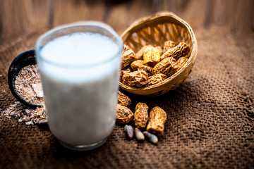 Close up of kharek or dried dates with raw milk in a transparent glass on brown colored surface with some powder of dried dates in a black colored clay bowl.