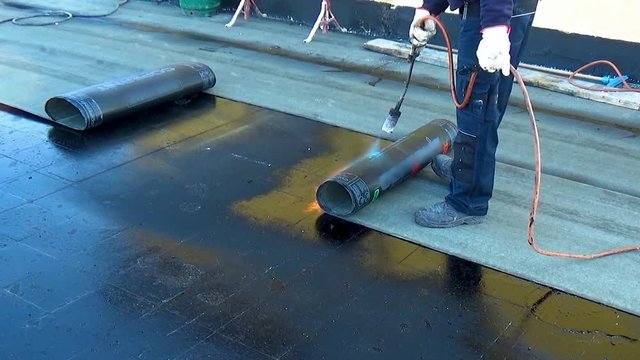 Worker performs sealing overlapping bitumen sheets on the flat roof of the building.