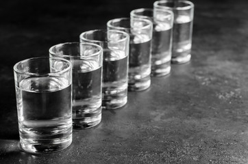 Glasses of vodka are in a row on dark background. Selective focus. Copy space