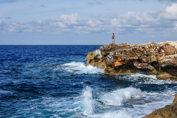 mother with baby in sling standing on rock and looking at the Mediterranean Sea