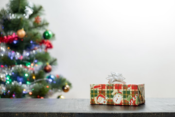 Christmas present on wood table and copy space. Front view of beautiful gift and decorated fir tree in blurred background
