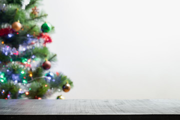 Christmas product background with blurred fir tree. Front shot of black wood table and backlit out of focus pine tree with garlands