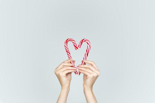 Love and kindness concept: hands hold two candy canes making the shape of heart. Heart formed of two white and red Christmas candies.