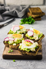 Avocado radish eggs bruschetta on cutting board. Selective fcous, space for text.