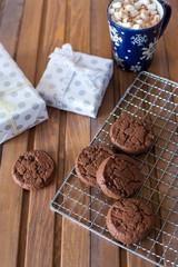 Chocolate cookies at metal grill, with napkin, cup of chocolate and present on wood background