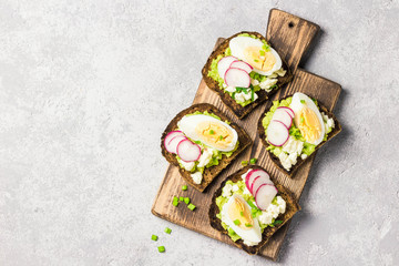 Whole grain toasted bread with smashed avocado radish eggs on cutting board. Top view, space for text.