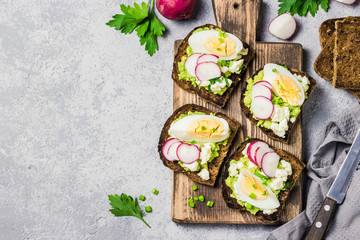 Whole grain toasted bread with smashed avocado radish eggs on cutting board. Top view, space for text.