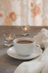 Cup of cocoa on a table, candles and knited blanket.