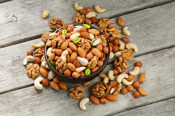 Wooden bowl with mixed nuts on a wooden gray background. Walnut, pistachios, almonds, hazelnuts and cashews, walnut.