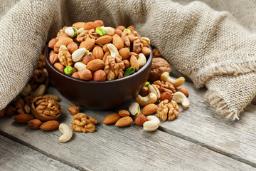 Wooden bowl with nuts on a wooden background, near a bag from burlap.