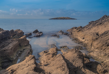 Mallorca, Balearic Islands, Spain - October 12, 2018: Long exposure on a rocky beach at low tide, with a small island in the background