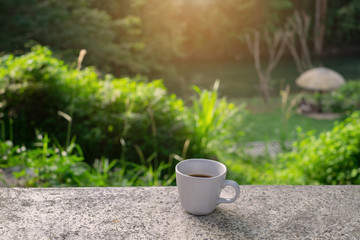 High angle view of a white cup of coffee on a table with blurred greenery in the background. 