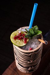 Alcoholic cocktail with lime, pomegranate and mint on a bar in a tiki bar.