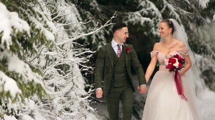 Young wedding couple walking, smiling and talking holding hands in snowy forest during snowfall. Winter wedding inspiration. Groom and bride having fun in fairy tale woods. Newlyweds at first meet.