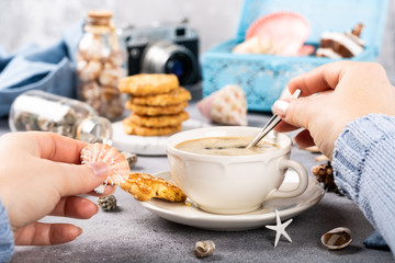 Woman hands with coffee and biscuits with seashells and decorations. Dreams of sea vacation and concept