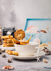 Cookie drops in cup of coffee with splash and biscuits, seashells and decorations. Dreams of sea vacation and concept. Copy space.