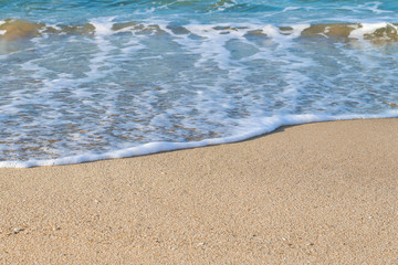 Closeup of a white sea foam on a yellow coastal sand on a sunny day. Marine background with copy space