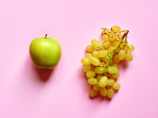 Above view of isolated set of a green apple with a bunch of sweet seedless grapes in studio with millennial pink background