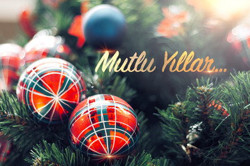 Closeup of shiny red bauble hanging from a decorated Christmas tree. Mutlu Yillar means Happy new year