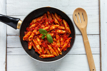 Sarten with bolognese macaroni, mint leaves and wooden spoon seen from above
