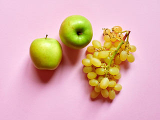 Above view of isolated set of a green apples with a bunch of sweet seedless grapes in studio with millennial pink background