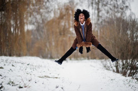 Curly hair african american woman wear on sheepskin coat and gloves posed at winter day, having fun and jump.