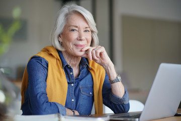  Beautiful senior woman looking pensive at home with laptop