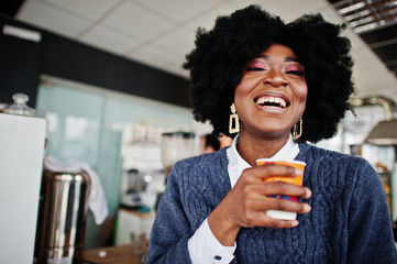 Curly hair african american woman wear on sweater posed at cafe indoor with cup of tea or coffee.