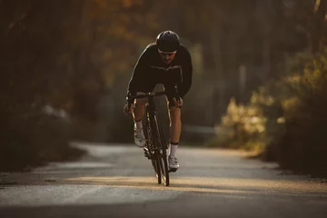 Rolgordijnen Professional road bicycle racer in action. Men cycling mountain road bike at sunset. © juananbarros