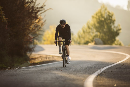 Professional road bicycle racer in action. Men cycling mountain road bike at sunset.