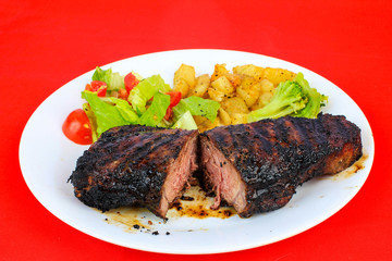 Medium Rare Sirloin Steak with Salad and Home Fries on Red Table