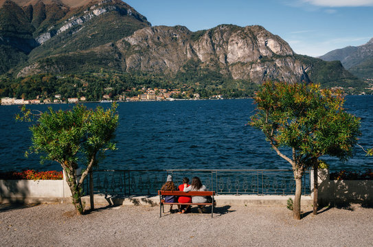 3 women sit on the bench and admire Como lake with Cadenabbia town, Italy.