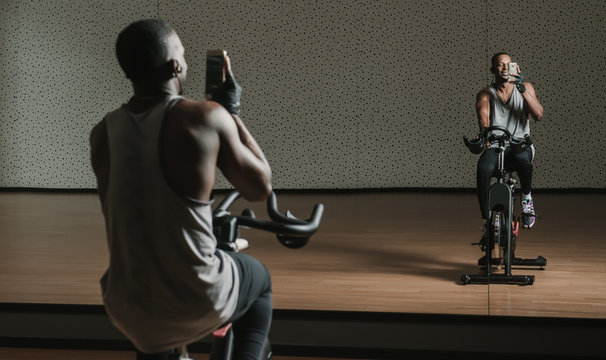 African American Man Making Selfie On Exercise Bike In Gym